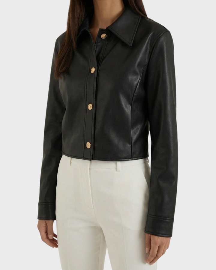 Luna Moda black faux leather cropped jacket with gold snap buttons worn by a model with white trousers.