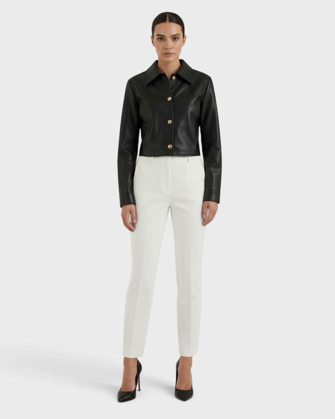Luna Moda Elettra black faux leather cropped jacket with snap buttons worn by a model with white trousers