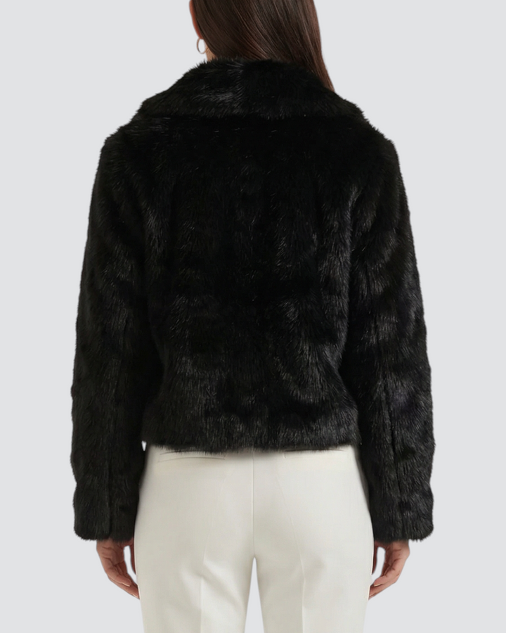 Luna Moda Debora black faux fur cropped jacket worn by a woman from the back, paired with white trousers and heels.