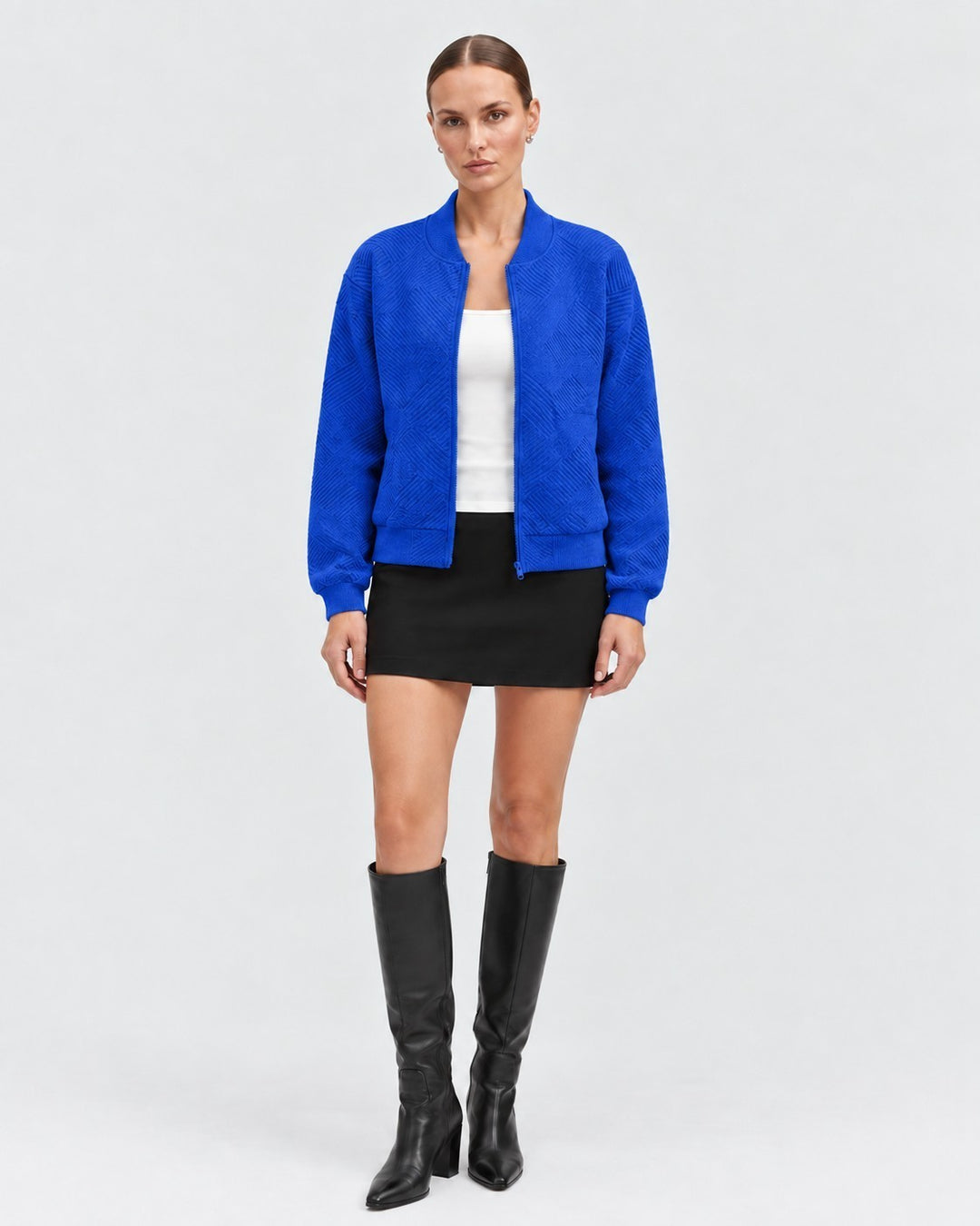 Luna Moda Dora bomber jacket in vibrant blue with a subtle geometric texture, worn with a black skirt and boots.