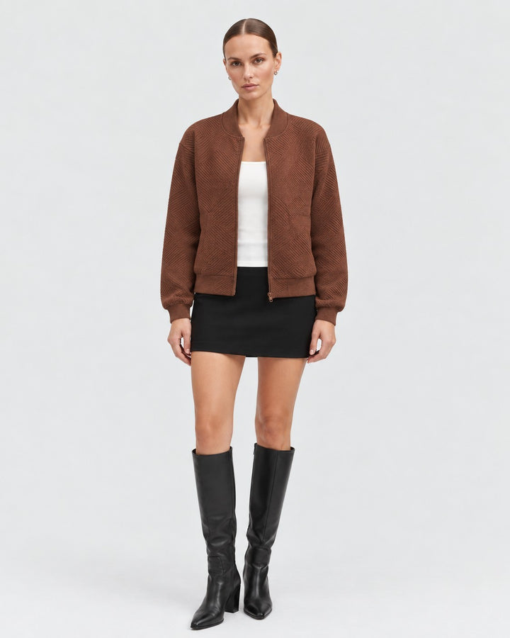 Luna Moda Dora bomber jacket in brown with a geometric pattern, worn by a model with a black skirt and tall boots.