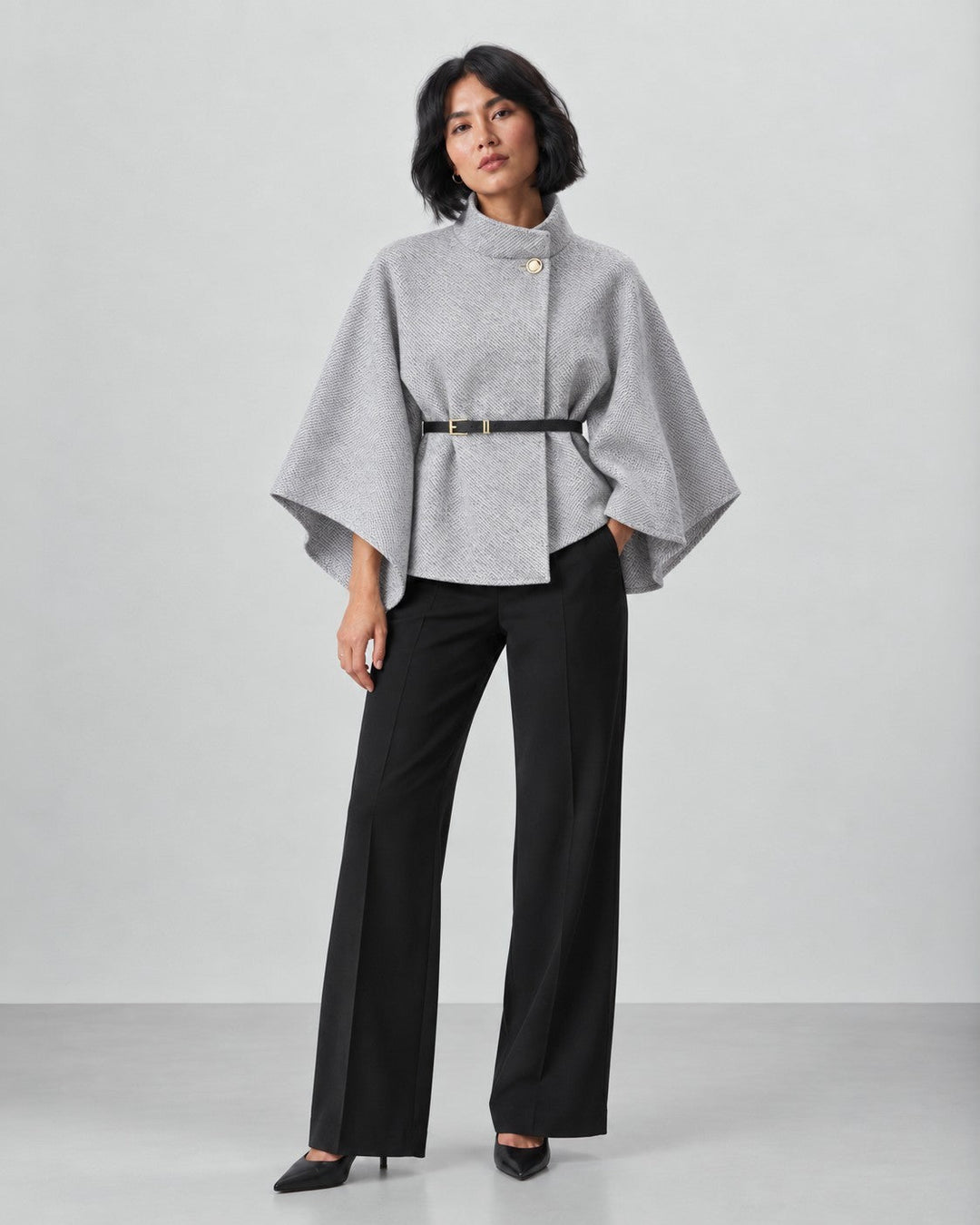 Model wearing a Luna Moda grey butterfly sleeve coat with a belted waist and black trousers against a neutral background