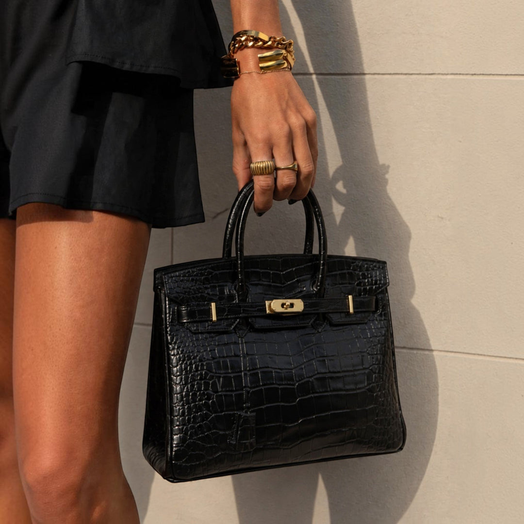 Luna Moda Ludovica black crocodile-embossed leather structured tote bag with gold buckle hardware held by a woman