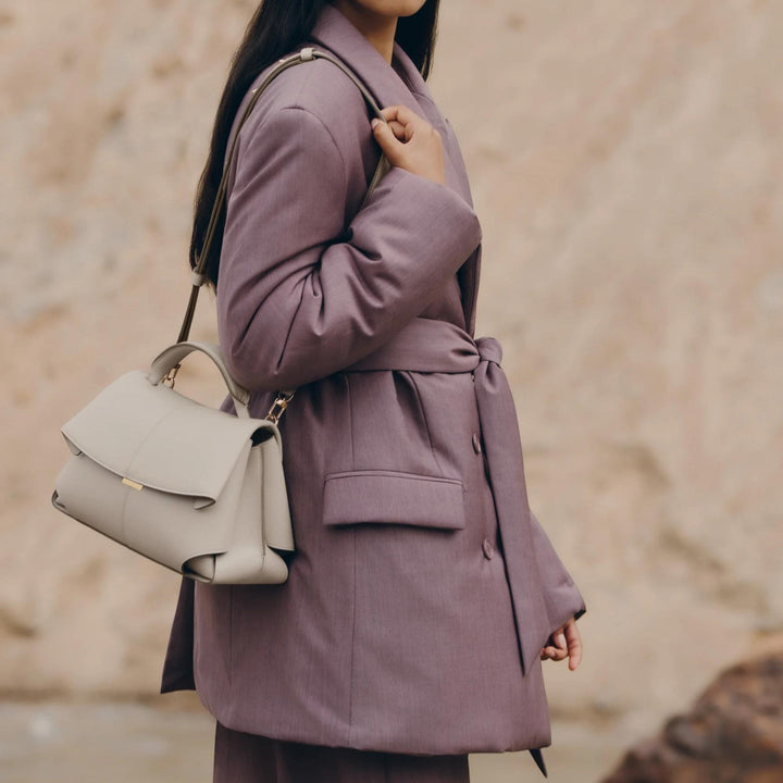 Luna Moda Lara minimal leather handbag in beige with adjustable shoulder strap worn by a woman in a mauve coat
