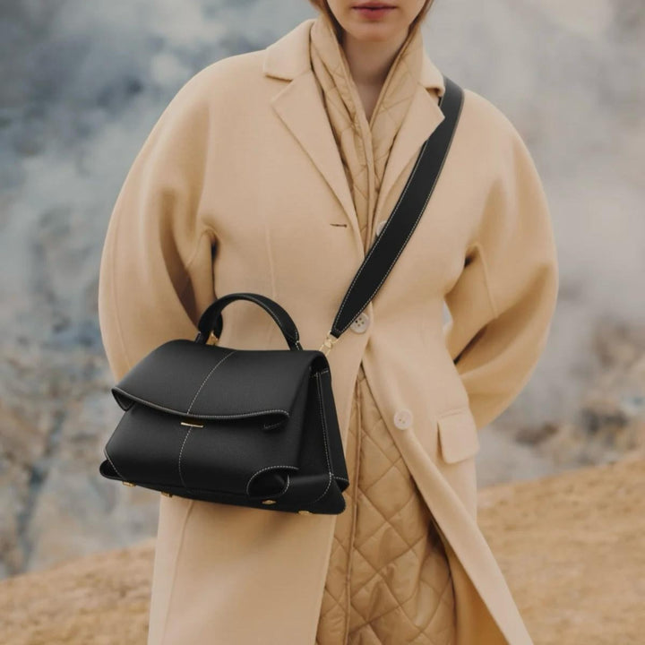 Luna Moda Lara black leather handbag with adjustable strap worn by a woman in a beige coat