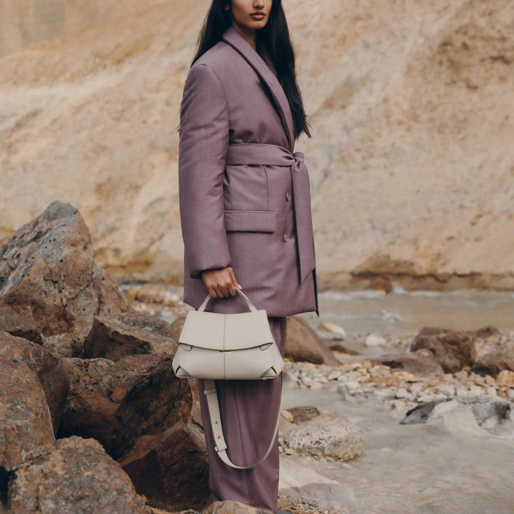 Luna Moda Lara minimal leather handbag in off-white held by a woman in a mauve suit outdoors