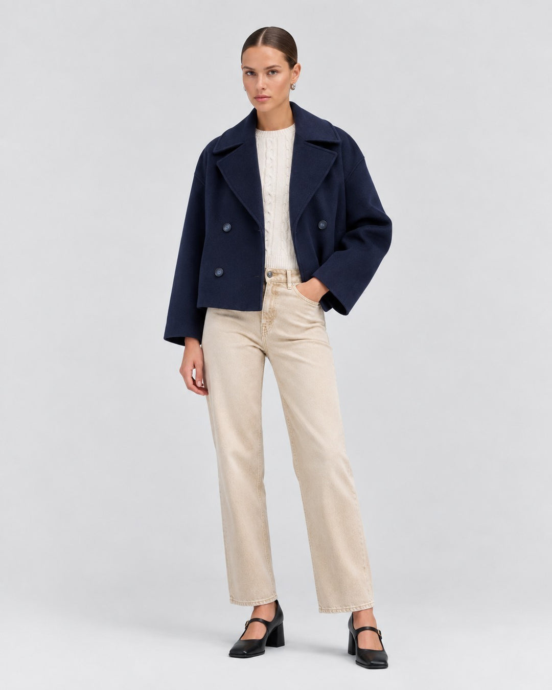 Model wearing a Luna Moda navy blue double-breasted short jacket over a white cable knit sweater and beige jeans.