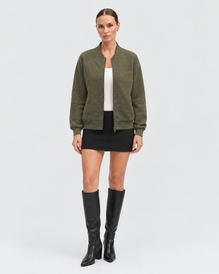 Luna Moda olive green bomber jacket with a geometric textured pattern, worn by a model with a white top and skirt.