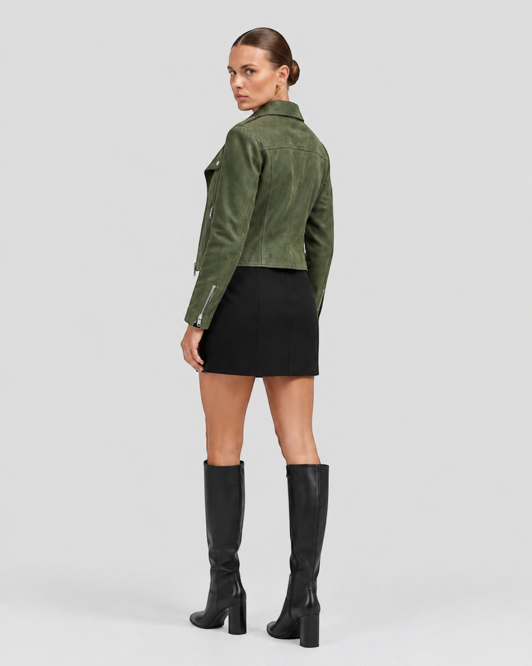Luna Moda biker jacket in olive green suede with silver zippers, worn by a model with a black skirt and tall boots.