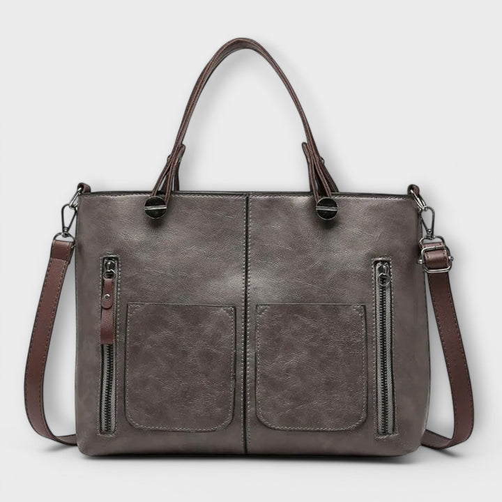 Luna Moda Olivera grey leather handbag with dual front zipper pockets, sturdy handles, and a detachable shoulder strap.