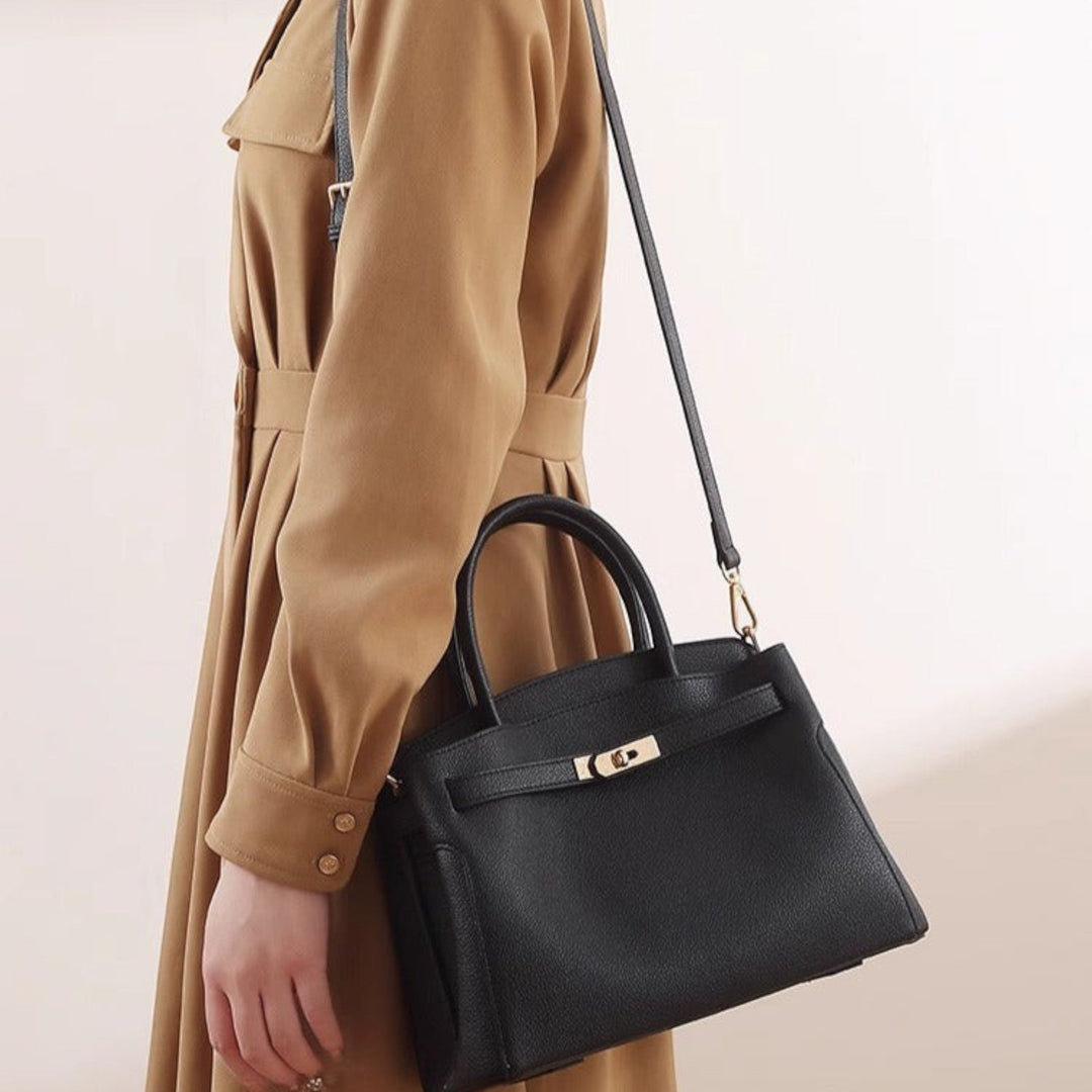 Luna Moda Orietta black structured handbag with gold turn-lock closure, carried by a woman in a tan dress.