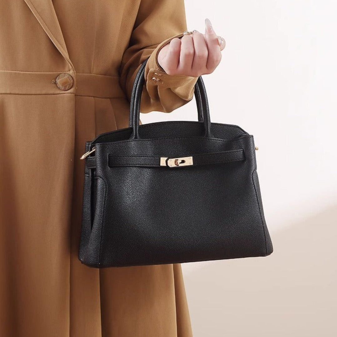 Luna Moda Orietta structured black handbag with gold-tone turn-lock closure and rolled top handles held by a model.