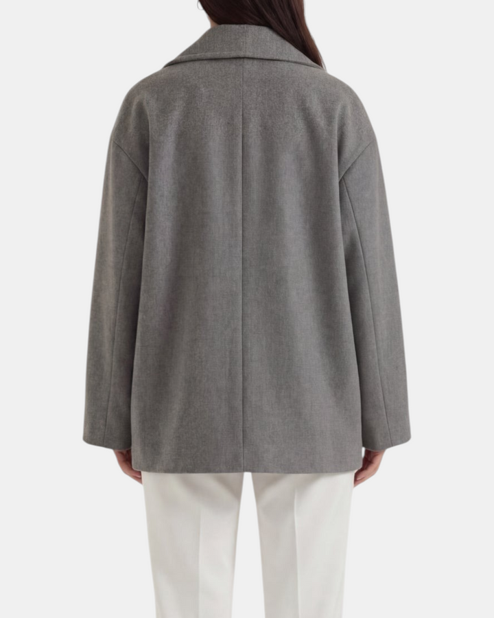 Luna Moda Corinna grey oversized coat with a relaxed fit worn by a woman with white trousers, back view