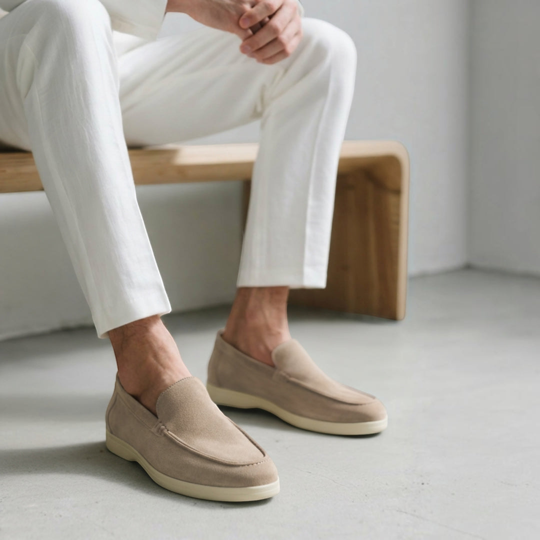 Luna Moda Romeo beige suede loafers with supportive insoles worn by a man in white trousers sitting on a bench.