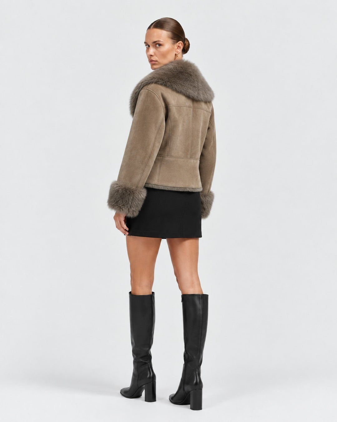 Luna Moda lambskin coat in taupe with a soft fur collar and cuffs, worn by a model in a black skirt and boots.