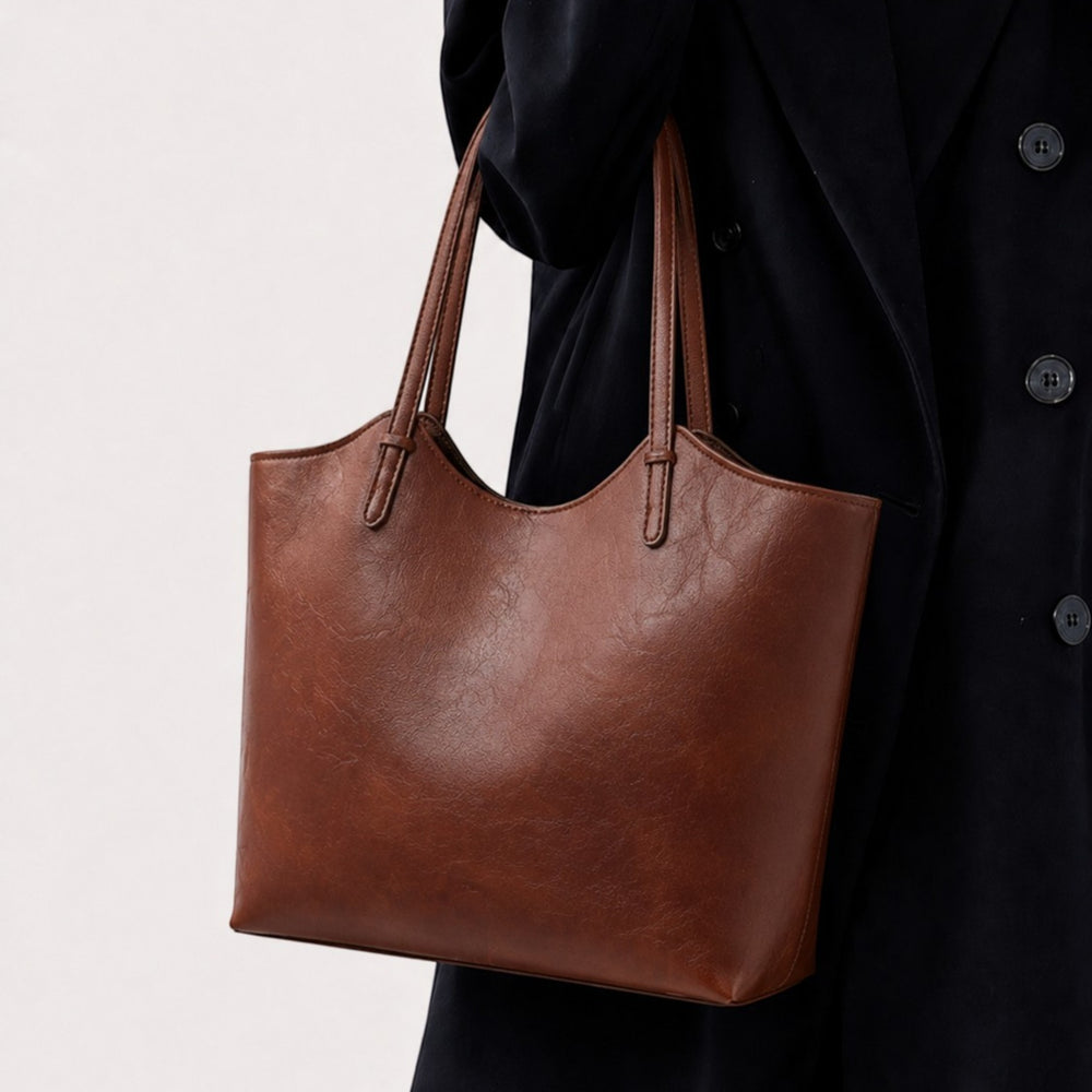 Luna Moda Thalassa brown faux leather tote bag with minimalist design held by a person in a dark coat