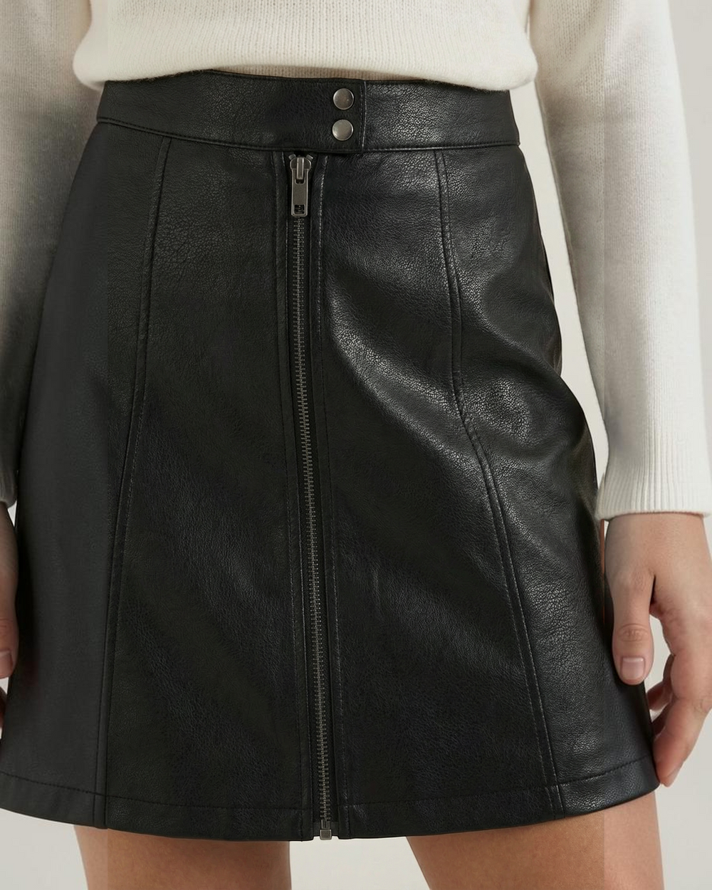 Luna Moda black vegan leather mini skirt featuring a front zip closure, architectural panels, and vertical stitching.
