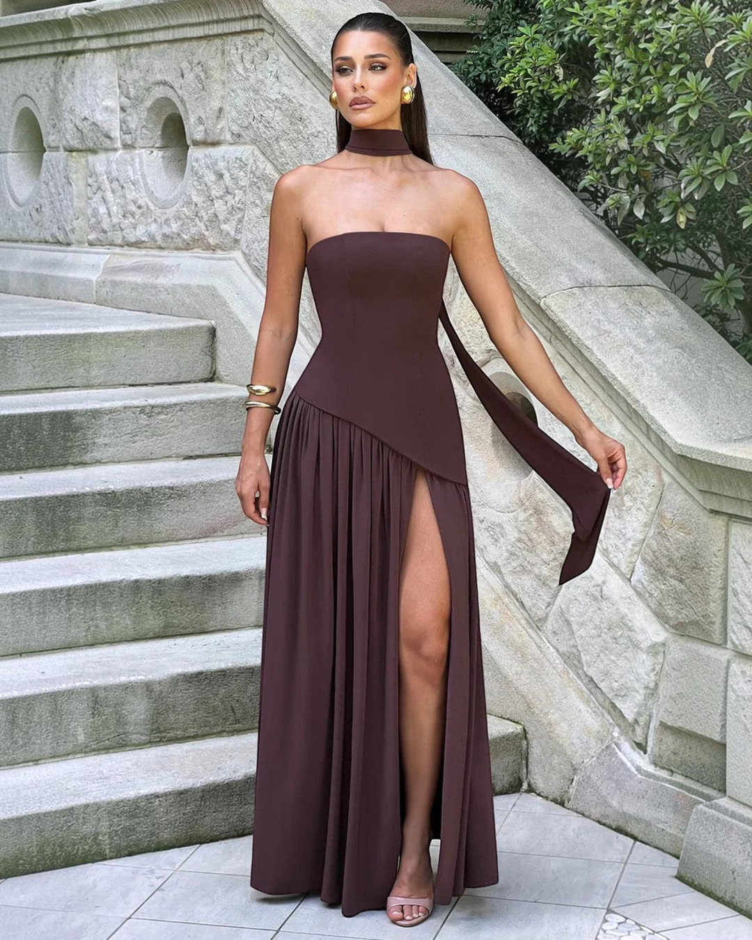 Luna Moda Zadie maxi dress in dark brown with a strapless bodice, choker detail, and high side slit on stone stairs