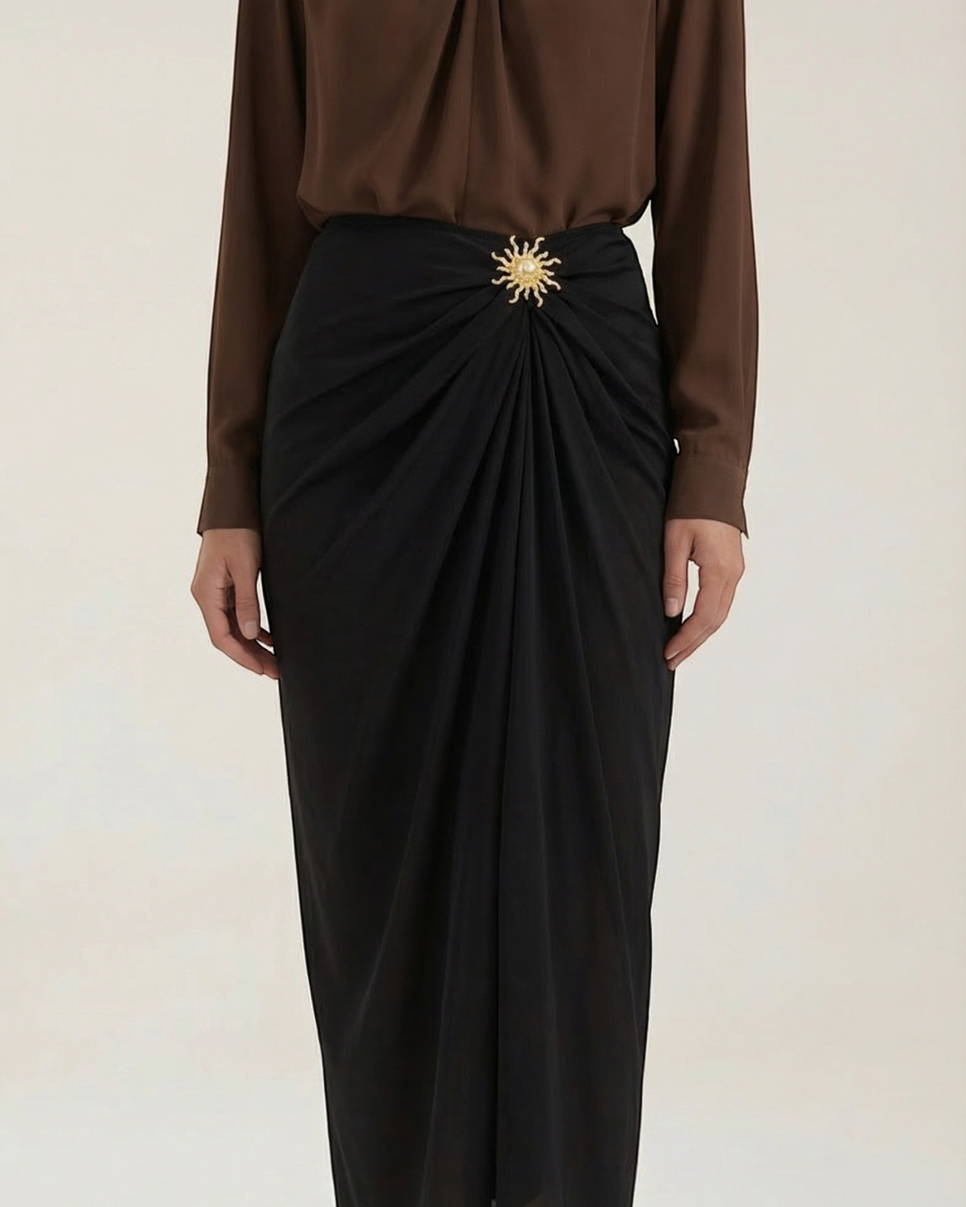 Luna Moda black midi skirt with elegant draping and a decorative gold sun-shaped brooch at the waist