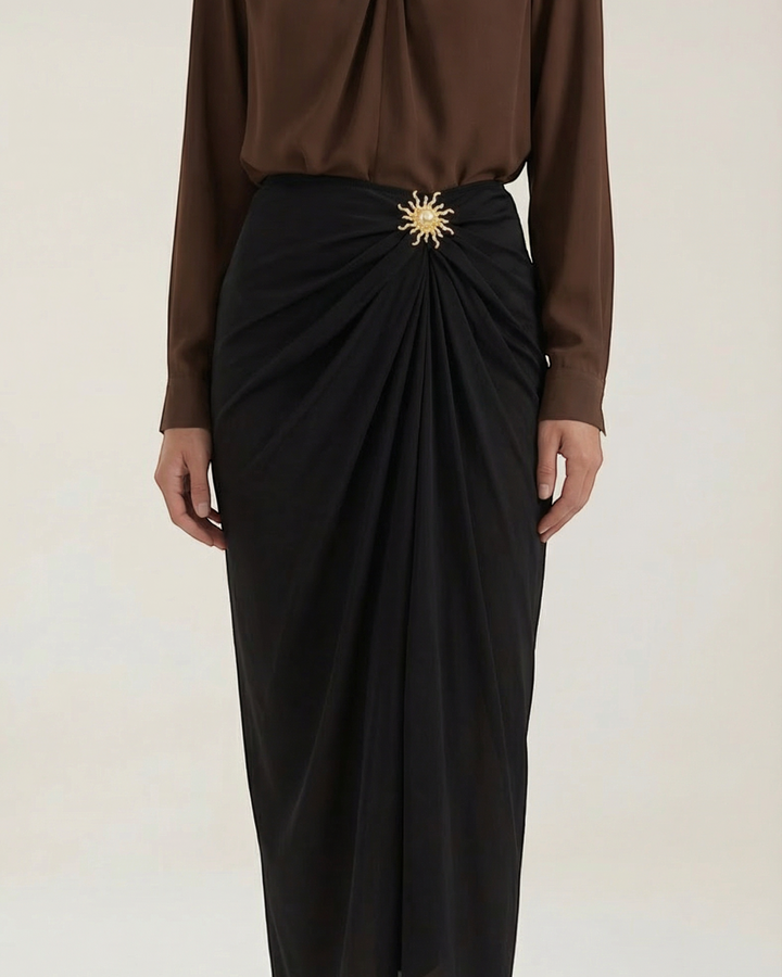 Luna Moda black midi skirt with elegant draping and a decorative gold sun-shaped brooch at the waist