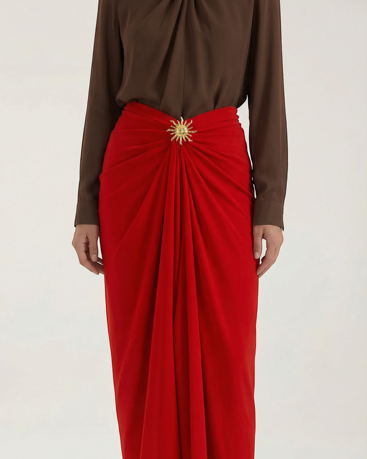 Luna Moda red midi skirt with elegant draping and a gold sun-shaped brooch worn with a brown blouse