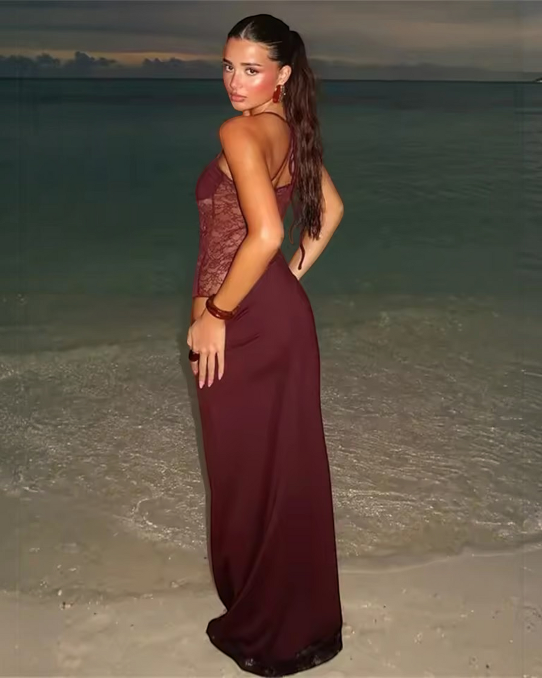 Luna Moda Giulia burgundy velvet evening dress with mesh details and strapless bodice worn by a model on the beach